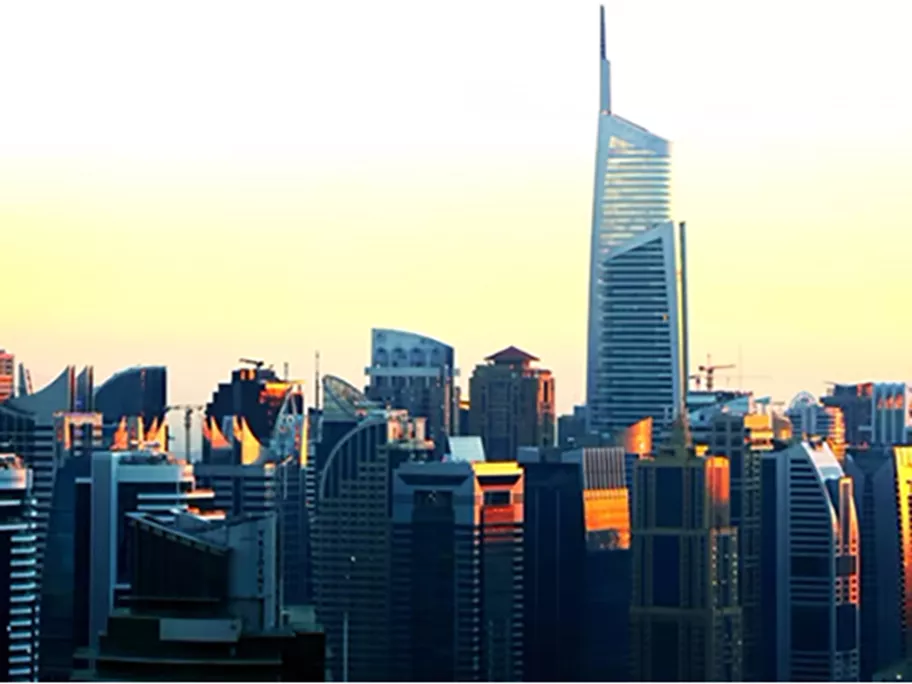 A vibrant cityscape of Dubai during golden hour, with the Almas Towers rising prominently above the skyline